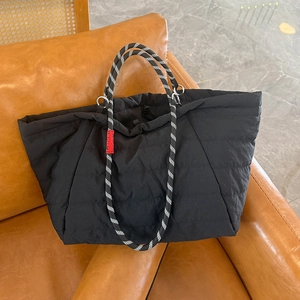 Detail of black quilted cloud tote bag with woven stripe handles on leather sofa