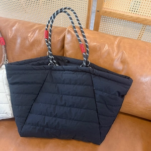 Detail of black quilted tote bag featuring woven rope handles and a red decorative label