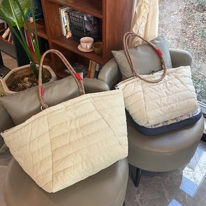 Detail of quilted tote bag with thick woven rope handles and red tag on a soft chair