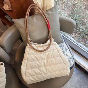 Detail of quilted puffer tote bag in cream white with braided rope handles and red tag