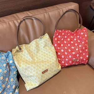 Close-up of three floral tote bags in blue, yellow and red with leather straps