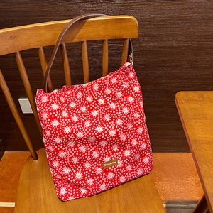 Detail of red floral tote bag with white star patterns and brown leather shoulder strap