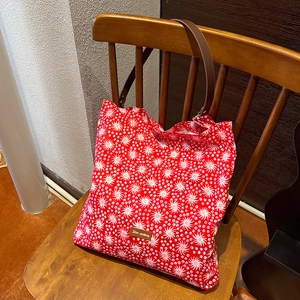 Detail of red floral canvas tote with leather patch and straps on a wooden chair