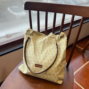 Close-up of floral tote bag with brown leather strap and brand label on a wooden chair