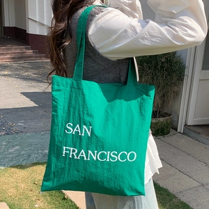 Back view of a woman carrying a bright green nylon tote bag with San Francisco lettering