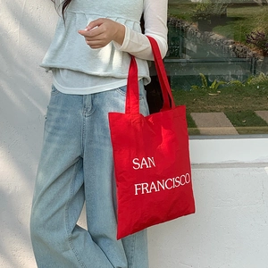 Vibrant red nylon tote bag featuring white San Francisco print shown on shoulder