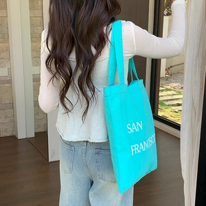 Close-up of a blue San Francisco print nylon tote bag carried on a model's shoulder