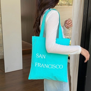 Detail of mint green nylon tote bag featuring white San Francisco lettering and dual straps
