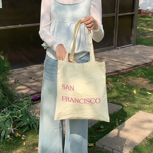 Detail view of cream nylon tote bag featuring red San Francisco print in outdoor sunlight