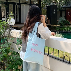 Detail of light blue nylon tote bag with pink San Francisco letter print in garden
