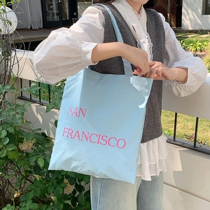 Detail of light blue nylon tote bag with pink San Francisco print on a casual outfit