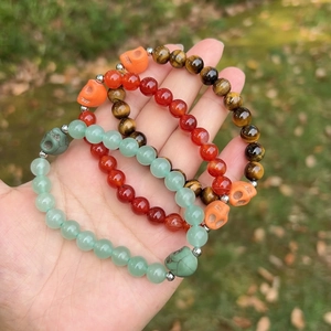 Three beaded bracelets with amethyst, tiger eye, and skull charms held in hand