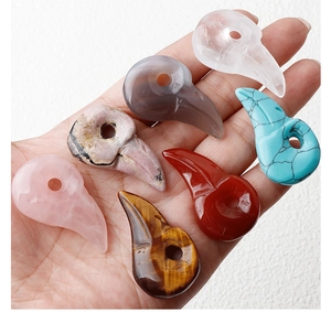 Detailed view of hand-held carved bird skull pendants in various natural crystal stones