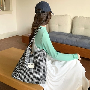 Detailed view of checkered canvas tote bag featuring 'SEE YOU' patch on the side