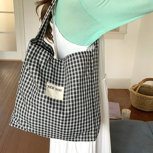 Detail of checkered tote bag featuring a stitched fabric label with SEE YOU text