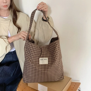 Detail of checkered tote bag with SEE YOU patch shown by model in warm home setting
