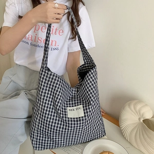 Close-up of black and white checkered canvas tote bag with See You patch and long strap