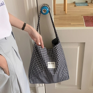 Detail of plaid canvas tote bag with See You label hanging on a door handle in bright room