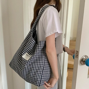 Detail of plaid canvas tote bag featuring white See You patch and shoulder strap design