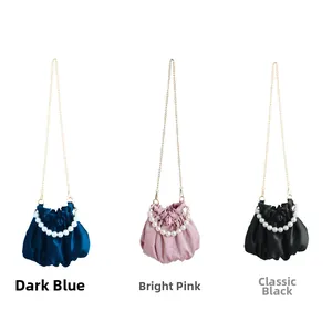 Three satin dumpling bags in navy, pink, and black with pearls and gold chains