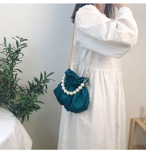 Dark green satin cloud bag with pearl handle and gold chain strap shown on a model