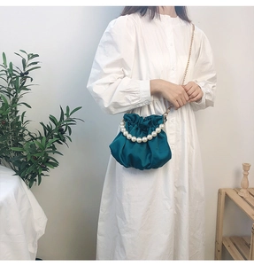 Close-up of emerald green pleated satin bag with pearl handle and gold chain strap