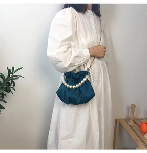 Detail of navy satin cloud bag with pearl handle and gold chain strap on model