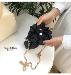 Detail showing the magnetic closure of a black satin pleated cloud bag with pearl