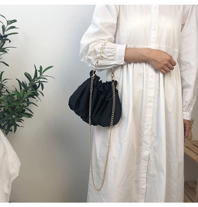 Detail of black pleated cloud bag with pearl handle and gold chain on model dress