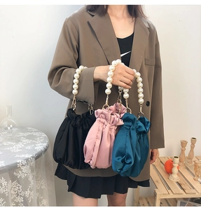 Close-up of three satin pleated bags in black, pink, and blue with elegant pearl handles
