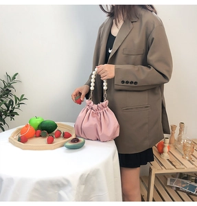 Close-up of pink pleated satin cloud bag with pearl handle held by a model