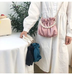 Detail view of satin cloud bag featuring large pearl handle and golden chain strap