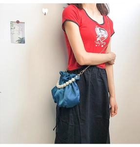 Blue satin drawstring bag with pearl handle and gold chain strap shown on a model