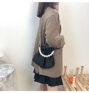 Detail of elegant black pleated satin bag with pearl handle and gold chain on model