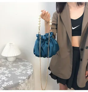 Detail of blue satin cloud bag with pearl handle and golden chain strap in soft lighting