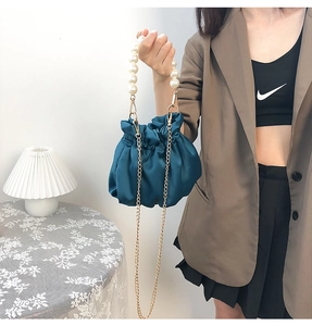 Detailed shot of dark teal satin cloud bag featuring large pearls and a gold chain