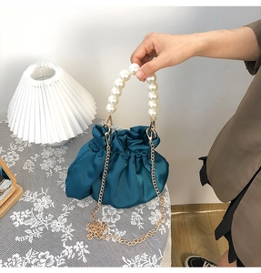 Detail of teal satin cloud bag with pearl handle and gold chain on lace tablecloth