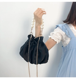Detail of black satin dumpling bag with pearl handle and gold chain on light blue dress