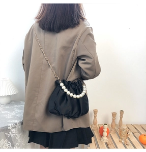 Detail view of black satin cloud bag with pearl strap on a person in cozy home setting