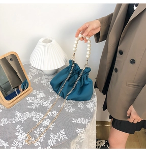 Lustrous lake blue satin cloud bag with large pearl handle and metal chain on model