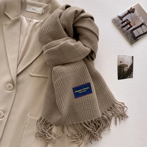 Close-up of brown plaid scarf with fringe detail and elegant fabric label on wool coat
