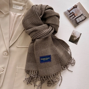 Close-up of thick plaid scarf with tassels and an Elegant & Classic fabric label