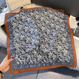 Detailed close-up of blue paisley square scarf with orange borders and smooth texture