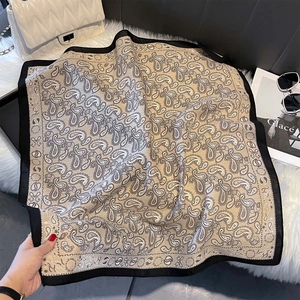 Detail of paisley print silk scarf with black border on plush rug with luxury accessories