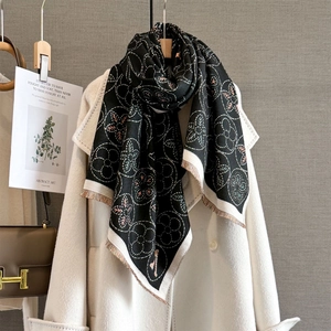 Détail de l'écharpe jacquard florale noire avec franges fines sur un manteau blanc