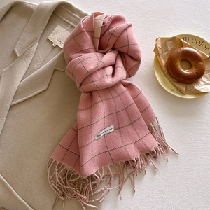 Detail of pink plaid scarf with long fringes paired with a beige coat in a cozy winter setting