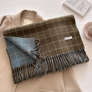 Detail of double-sided plaid scarf with fringe on a beige wool coat in olive and grey