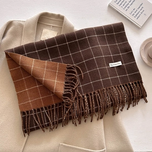 Detail of coffee plaid cashmere-like scarf with fringe and white woven label on coat