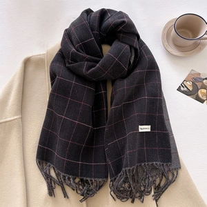 Detail of dark grey plaid scarf with fringes and white label on a cozy winter background