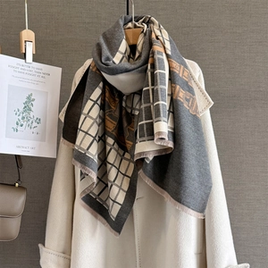Gros plan d'une écharpe à carreaux gris et beige avec motifs orange et franges
